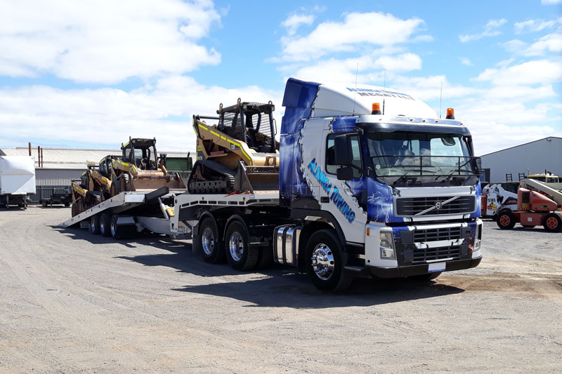 A tilt tray Tow truck carrying two earthmowing machines