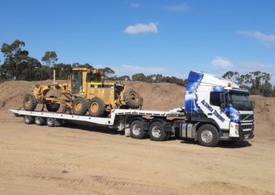 A large tilt tray truck transporting large roadwork machinery in Adelaide